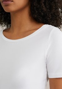 T-shirt din bumbac alb, cu guler rotund și mâneci scurte, textură netedă, design ajustat și detalii de cusătură minime.