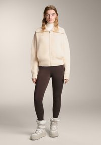 Kényelmes krémszínű cipzáros polárdzseki, testhez simuló barna leggings és fehér szőrmével bélelt csizma. A puha anyag és a laza szabás fokozza a kényelmet.