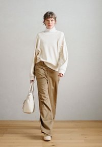 Suéter crema, pantalones beige, bolso crema. El suéter tiene un ajuste relajado, los pantalones son a medida, el calzado es simple y de color claro. Suelo de madera.