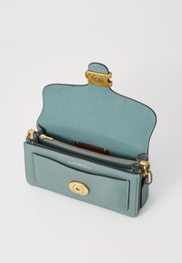 Tealte leren tas met gouden hardware. Beschikt over een ritssluiting, een interne kaartsleuf en een haaksluiting. Soepele textuur en gestructureerde vorm.