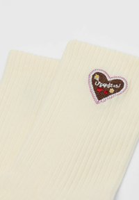 Cream ribbed socks with a small sewn heart patch featuring daisies, red hearts, and white text in cursive.