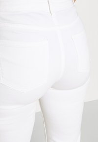 Jeans de mezclilla blanca con cintura alta y dos bolsillos en la parte trasera. Textura suave con detalles de costura mínimos y un diseño ajustado.