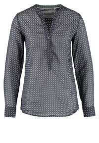 Blouse bleu marine à manches longues avec de petits motifs circulaires blancs et une patte de boutonnage partielle à l'avant.