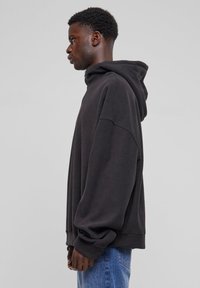 Overdimensioneret sort hættetrøje med snorlås, brede ærmer og ribbet manchetter, parret med blå denim jeans. Blødt, struktureret stof.