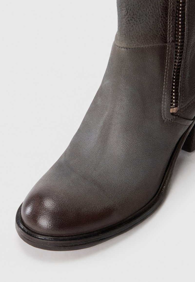 Stivale alla caviglia in pelle marrone scuro con zip laterale e tacco basso su sfondo bianco, vista frontale e laterale.