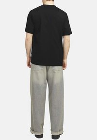 Camiseta de algodón negra combinada con jeans de pierna ancha en gris claro. La camiseta tiene un cuello redondo clásico y mangas cortas. Detalles mínimos.