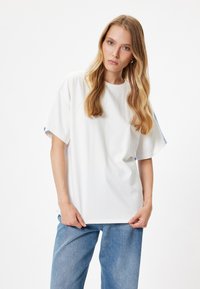 Hvid bomulds T-shirt med løs pasform og korte ærmer, med blå accenter på sidesømmene. Afslappet design og blød tekstur.