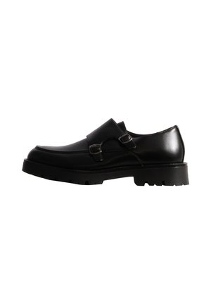 Mocassin en cuir noir avec deux brides à boucle et une semelle épaisse crantée, présenté de profil sur un fond blanc.