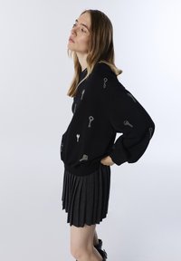 Czarna, oversize bluza z kapturem z srebrnymi wzorami kluczy, zestawiona z plisowaną, ciemnoszaro spódnicą. Miękka tkanina, luźny krój i ściągacze.