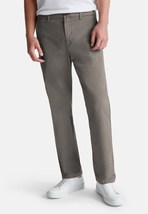 Chinos gris en tissu léger, au design droit, avec fermeture à bouton et poches latérales, portés avec des baskets blanches.
