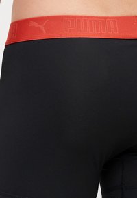 Black athletic shorts with a smooth texture feature a red elastic waistband embossed with "PUMA" and logo.