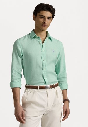 Camicia verde chiaro a maniche lunghe con bottoni realizzata in tessuto strutturato. Presenta un piccolo logo sul petto ed è abbinata a pantaloni bianchi e una cintura marrone.