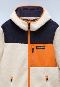 Giacca in pile con corpo crema, parte superiore blu navy e dettagli arancioni. Presenta una tasca con zip, colletto alto e tessuto strutturato.