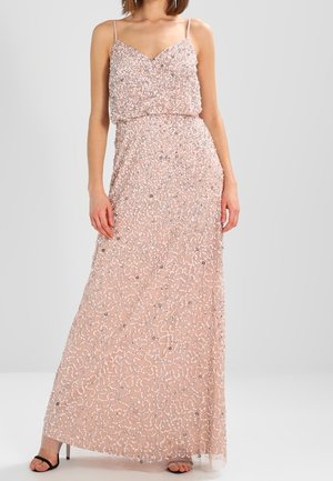 Vrouw draagt een mouwloze, blush roze, vloerlange jurk met zilveren pailletten en dunne bandjes, gecombineerd met zwarte open-toe hakken.