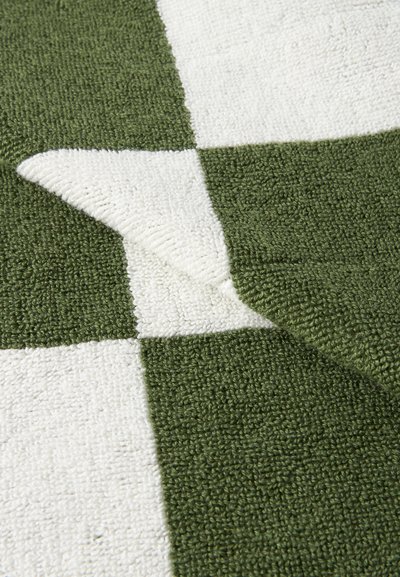 Ύφασμα με πράσινο και λευκό καρό υφή, με μια γωνία διπλωμένη προς τα πίσω, δείχνοντας την ανάποδη πλευρά του μοτίβου.