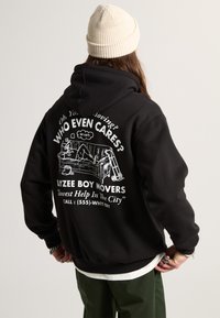 Sudadera negra con un estampado gráfico en la espalda que presenta un texto y unas ilustraciones humorísticas relacionadas con el movimiento. Acentos en blanco, corte holgado.