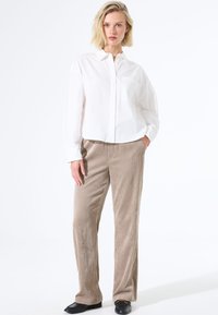 Witte overhemd met lange mouwen en een borstzak, gecombineerd met beige ribfluwelen broek. De broek heeft verticale strepen en een rechte snit.