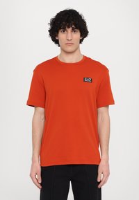 Short-sleeve, crew-neck t-shirt in bright orange cotton, featuring a small black EA7 logo patch on the left chest area.