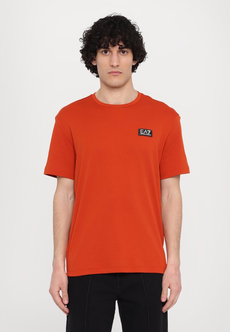 Short-sleeve, crew-neck t-shirt in bright orange cotton, featuring a small black EA7 logo patch on the left chest area.