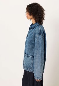 denim jakna v svetlo modri barvi, ki ima širok ovratnik, zapenjanje na gumbe spredaj in velik sprednji žep. Prijeten kroj in teksturirana tkanina.