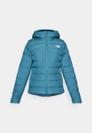 Teal pufferjack met een ritssluiting aan de voorkant en een capuchon, voorzien van doorstikking en een logo op de linkerkant van de borst. Soepele textuur en lichtgewicht ontwerp.
