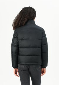 Sort pufferjakke med høj krave, med horisontalt quiltet design og elastiske manchetter, parret med mørke jeans. Glat, skinnende tekstur.