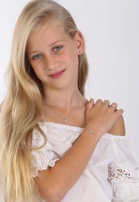 Silbernes Schmuckset mit einer Halskette mit Anhänger, passendem Armband und Ring. Das Mädchen trägt ein weißes schulterfreies Oberteil mit Spitzenakzenten.