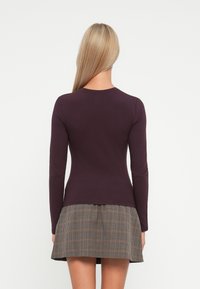 Langärmliges Oberteil aus dunkelviolettem Baumwollstoff, kombiniert mit einem karierten Rock in flared Design in Brauntönen und Beige.