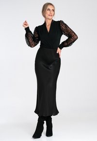 Schwarzes Kleid mit taillierter Oberseite und fließendem Satinrock. Verfügt über transparente, schwarze Puffärmel mit Leopardenmuster und einen hohen Ausschnitt.