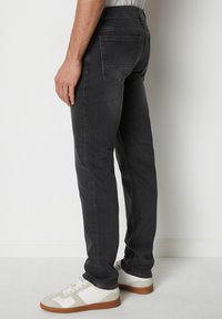 Ciemnoszare dżinsy o dopasowanym kroju, z tylną kieszenią i subtelną teksturą. Połączone z białymi i szarymi sneakersami.