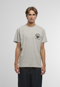 Tricou din bumbac gri, cu mâneci scurte, decolteu rotund și imprimeu grafic negru pe partea stângă a pieptului. Croială lejeră și textură moale.