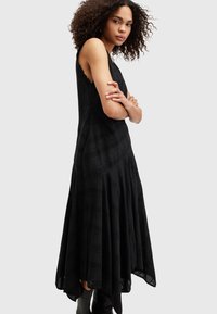 Vestido negro sin mangas con escote de ondas, diseño en capas con forma de A, tela texturizada y patrones de bordado intrincados en todo el vestido.