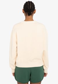 Cremfarbener Sweatshirt mit lockerer Passform, gerippten Bündchen und Saum; getragen mit grünen Shorts und zeigt ein einfaches, minimalistisches Design.