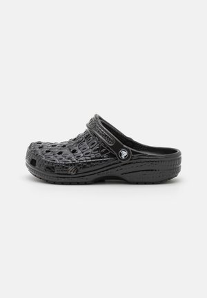 Sabot noir à enfiler avec motif crocodile texturé, trous de ventilation et bride réglable au talon, présenté de profil sur un fond blanc.
