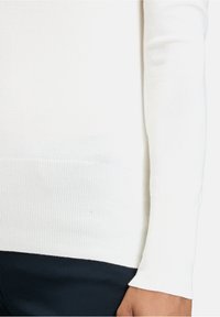 Weißer, ribbeliger Strickpullover mit Rundhalsausschnitt und langen Ärmeln, der eine glatte Textur und einen taillierten Saum aufweist.