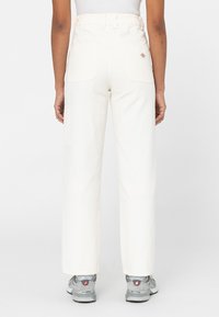 Crème kleurige high-waisted broek met rechte pijpen, voorzien van twee achterzakken en een zijzak, gecombineerd met grijze sneakers.