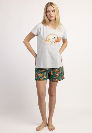 Mujer de pie descalza con camiseta gris claro con estampado de animales y pantalones cortos verdes con patrones de animales de la jungla y hojas.