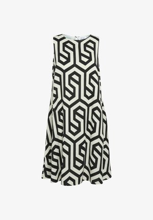 Mujer con un vestido sin mangas de patrón geométrico en blanco y negro y zapatillas de plataforma color crema, de pie con las piernas separadas.