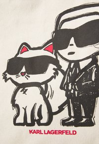 Kokvilnas iepirkumu soma ar multfilmu ilustrāciju, kurā attēlots figūra un kaķis saulesbrillēs, ar melniem kontūriem un rozā akcentiem, ar uzrakstu "Karl Lagerfeld".