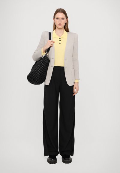 Gray blazer over a yellow polo with button details, paired with black wide-leg trousers and black textured bag. Chunky black shoes complete the look.