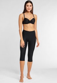 Black capri leggings made from stretch fabric, featuring a smooth texture and fitted design, paired with a black padded bra.