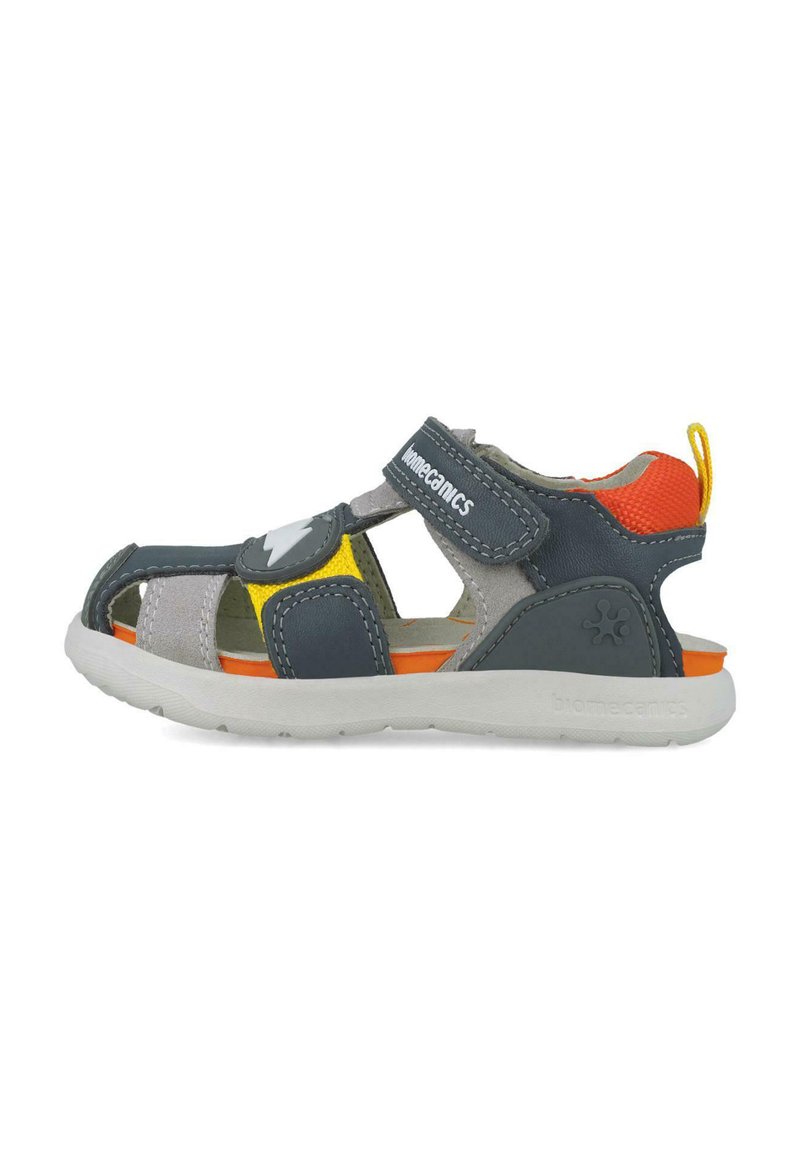 Sandal gris y marino con acentos en naranja, amarillo y gris. Correa ajustable de Velcro, diseño de punta abierta y suela de goma texturizada.
