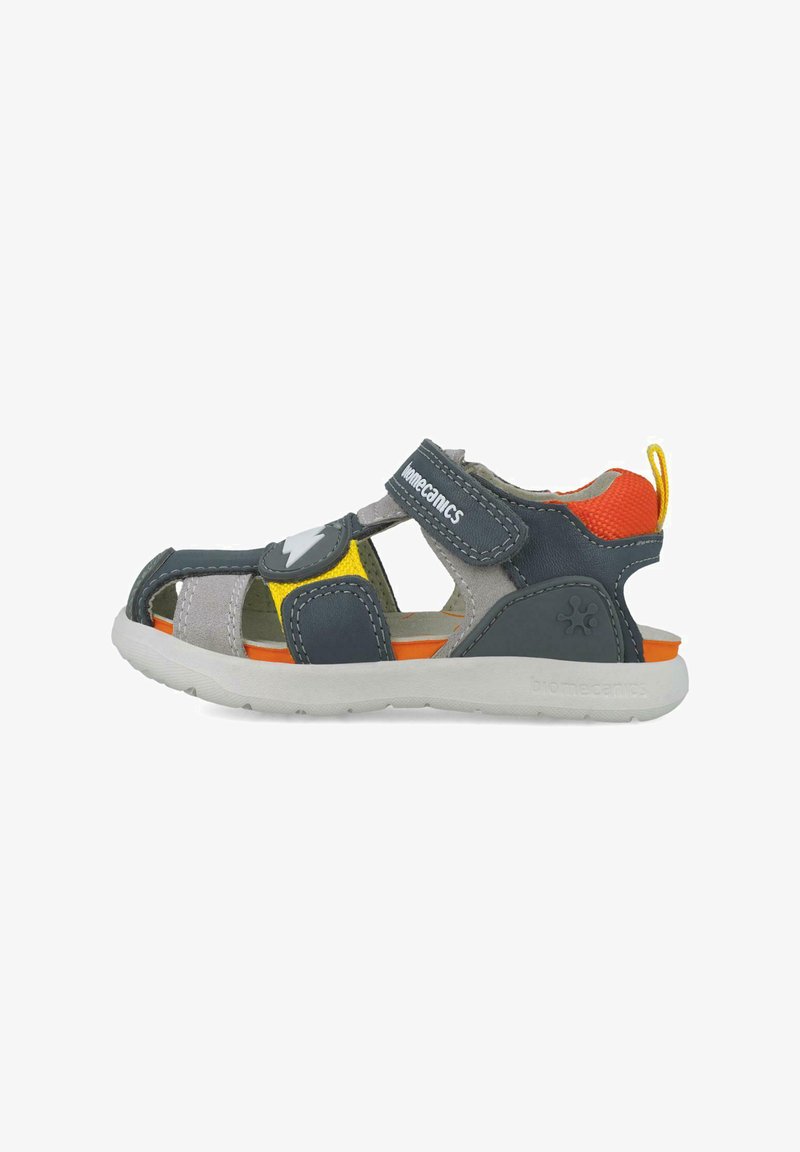Sandal gris y marino con acentos en naranja, amarillo y gris. Correa ajustable de Velcro, diseño de punta abierta y suela de goma texturizada.