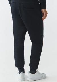 Sorte sweatpants lavet af blødt stof, med en afslappet pasform, ribafslutning ved anklerne og en baglomme. Kombinationen med hvide sneakers.