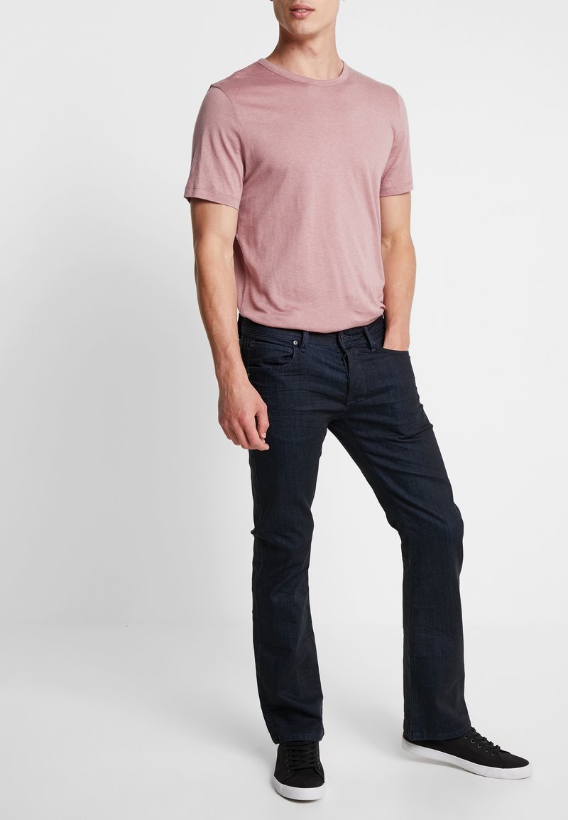 Camiseta de manga corta rosa claro combinada con jeans azul oscuro y zapatillas negras. El conjunto presenta un ajuste casual y texturas suaves.