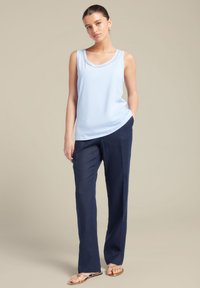 Lichtblauw mouwloos topje met een ronde hals, gecombineerd met donker marineblauwe rechte broek en tan platte sandalen. Gladde stofstructuur.