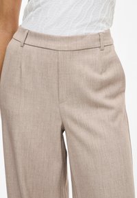 Μπεζ tailored παντελόνια με λεία υφή, μεσαία μέση και πτυχές μπροστά. Σχεδιασμένα για ίσια γραμμή.