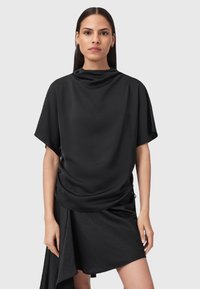 Top nero con scollo drappeggiato e maniche corte, realizzato in un tessuto liscio. Accompagnato da una gonna nera asimmetrica con un orlo fluente.