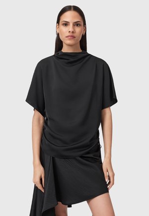 Top nero con scollo drappeggiato e maniche corte, realizzato in un tessuto liscio. Accompagnato da una gonna nera asimmetrica con un orlo fluente.