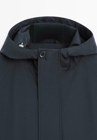 Dunkelgraue wasserdichte Jacke mit hohem Kragen, Knopfverschluss und verstecktem Reißverschluss unter der Blende.